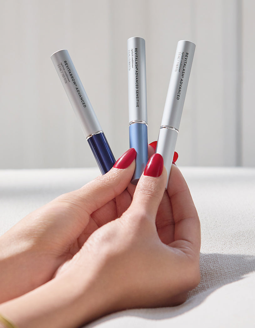 Three serums held by a hand with red nail polish against a neutral background